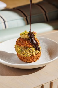 Pistachio profiterole dessert topped with warm chocolate sauce at Azzurra Chelsea, combining classic Italian pastry techniques with modern presentation.