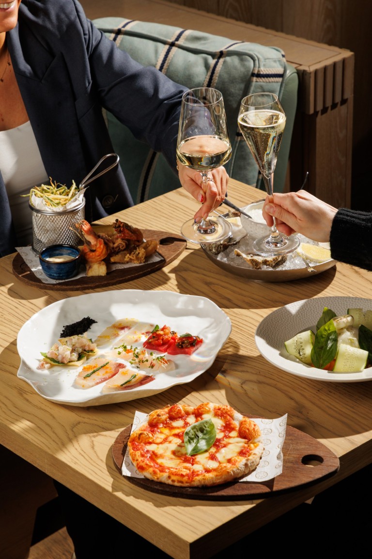 Guests enjoying a luxury Italian dining experience at Azzurra Chelsea, featuring seafood dishes, oysters, pizza and fine wine in an elegant Chelsea restaurant setting.